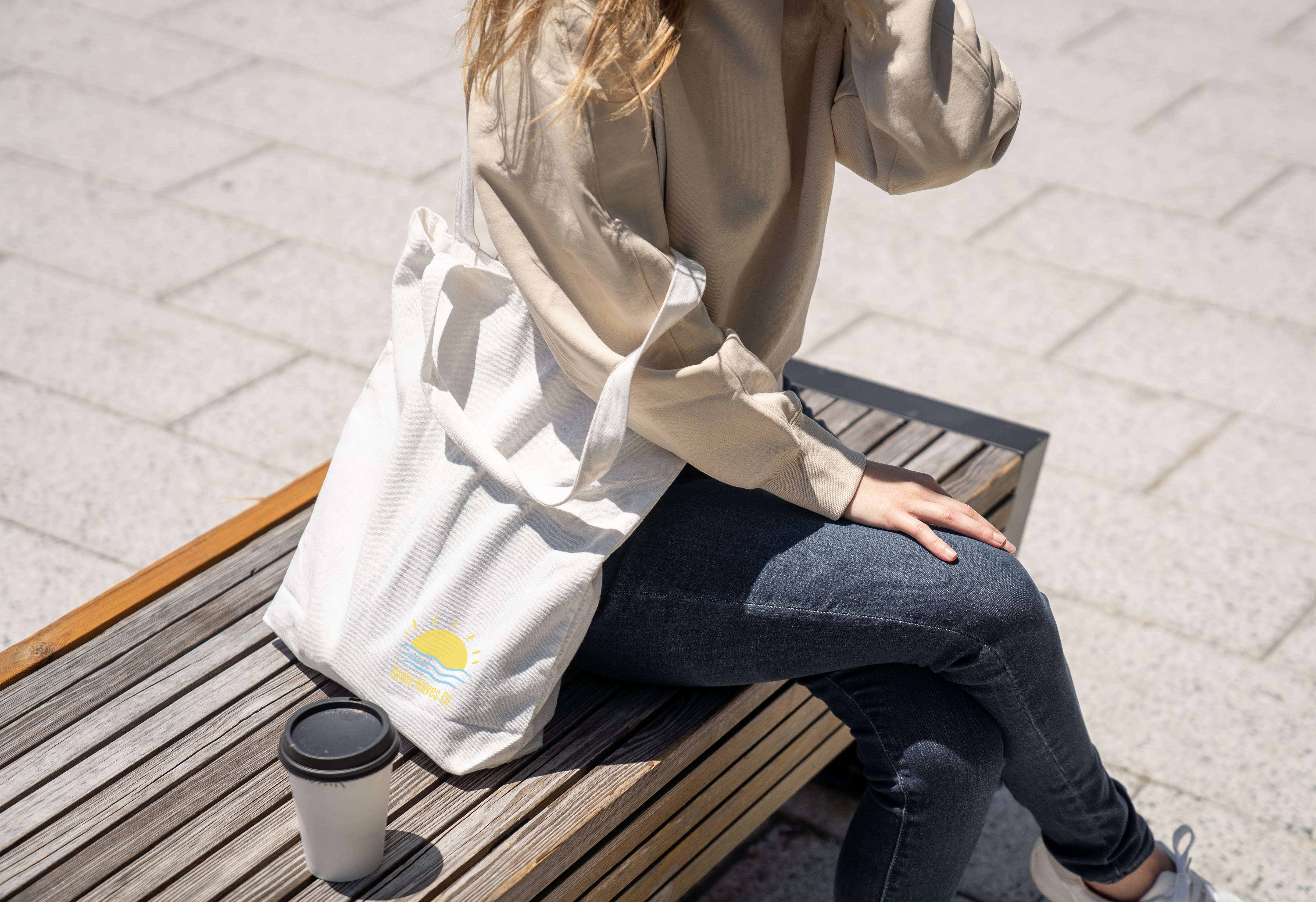 Person sitting on bench with custom-printed tote bag and coffee